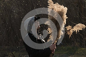 A girl on the background of reeds in the field, holding branches of reeds in her hand.