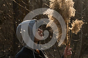 A girl on the background of reeds in the field, holding branches of reeds in her hand.