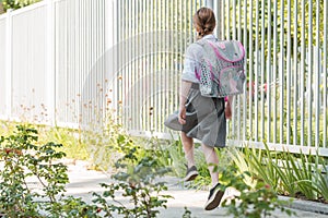 Girl with a backpack goes along the sidewalk to school on a sunny day