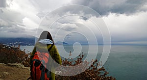 The girl with the backpack looks into the distance in the sea and the mountains. The focus in the background