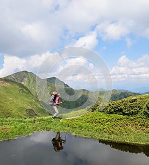 Girl with backpack is reflected in mountain lake