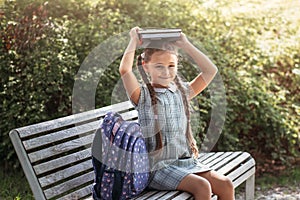 Girl with a backpack sitting on a bench and holds  books near the school. Back to school, lesson schedule, a diary with grades.