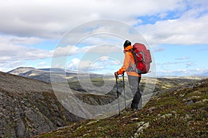 Girl with backpack standing on top of a mountain and looking for