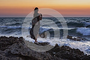 A girl with a backpack stands against the sea. A lone traveler admires the sunset