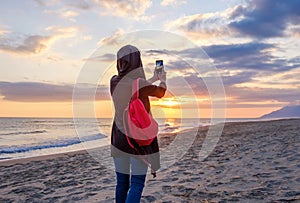 A girl with backpack takes foto a sunset on a mobile phone camera on the beach, Patara Beach, Turkey