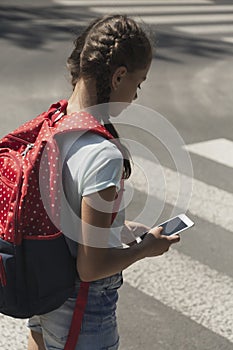 Girl using smartphone while walking through crosswalk to the school