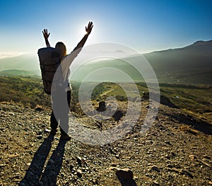 Girl-backpacker with hands up in the mountains