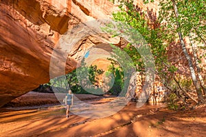 Girl Backpacker walking under Natural Bridge Arch Coyote Gulch