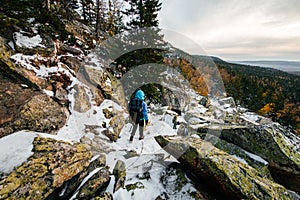 a girl with backpacks walks on rocks in the snow