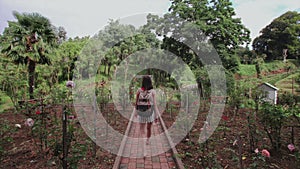 Girl with bag walks through garden in tropical park, palms, coniferous trees, flower plantation