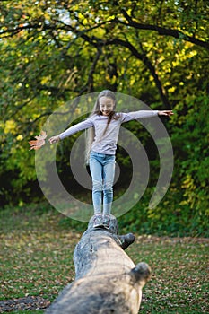 A girl balances on a fallen log with a leaf in her hand