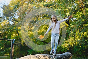 A girl balances on a fallen log with a leaf in her hand