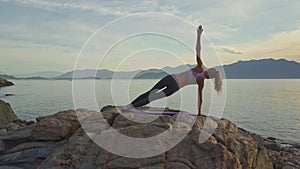 Girl balances on right arm in yoga pose on beach at dawn