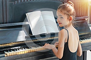 Girl ballerina playing the piano in the morning at home. Child so cute girl looking at something on the piano with sun