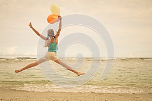 Girl with balloons jumping on the beach