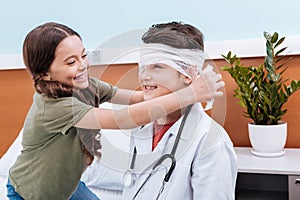 girl bandaging boy doctor's head in hospital