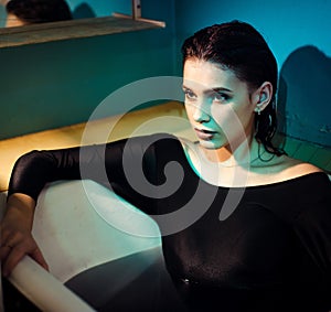 Girl with bare shoulders lying in the bathroom with colored purple water. Fashion concept