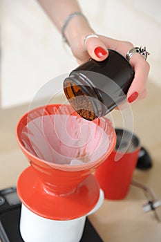 Girl barista pours freshly ground coffee from manual coffee grinder into red pouver with paper filter closeup