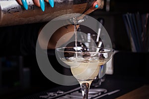 Girl bartender pours cocktail into glass. Close-up.