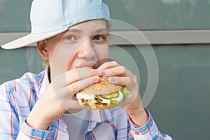 Girl in a baseball cap eats a hamburger with meat, front view, close-up