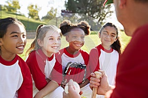 Girl baseball team in a team huddle listening to the coach