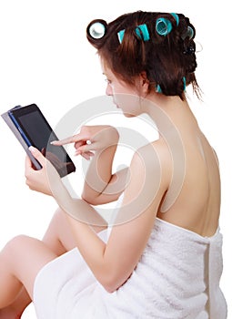 Girl in a bath towel and hair curlers with tablet computer in her hands.