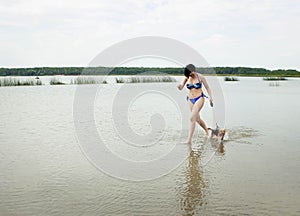 A girl in a bathing suit runs across the lake with a Yorkshire Terrier dog. The frame is in motion