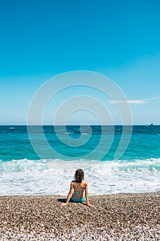 A girl in a bathing suit sits on the beach and looks at the sea