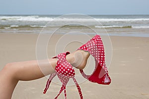 Girl on Beach holding bikini with her leg