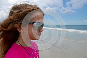 Girl on beach looking out to the ocean with waves reflecting in her sunglasses