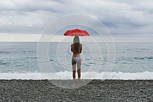 Girl on beach with red umbrella in front of a stormy sky