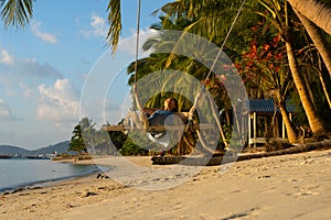 The girl on the beach rides on a swing during sunset. Sunset in the tropics, enjoying nature. Swing tied to a palm tree by the