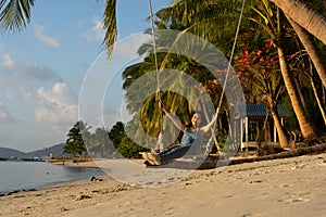 The girl on the beach rides on a swing during sunset. Sunset in the tropics, enjoying nature. Swing tied to a palm tree by the