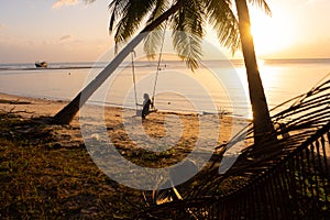 The girl on the beach rides on a swing during sunset. Sunset in the tropics, enjoying nature. Swing tied to a palm tree by the