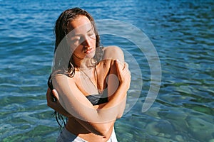 Girl on the beach with wet hair, beautiful figure and clean skin against the sea in sunny weather