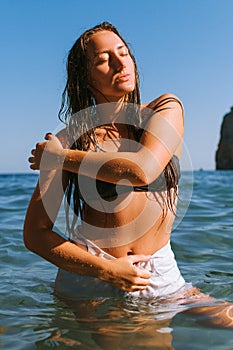 Girl on the beach with wet hair, beautiful figure and clean skin against the sea in sunny weather