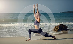 A girl on the beach in yoga Virabhadrasana pose. Yoga at sunrise.