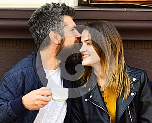 Girl and bearded guy have coffee on brown terrace background.