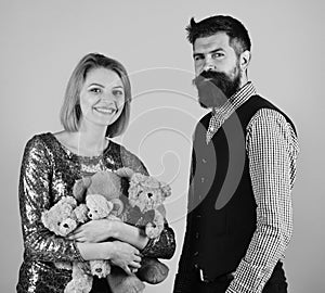 Girl and bearded man with happy faces play with soft toys. Couple in love holds heap of teddy bears on blue
