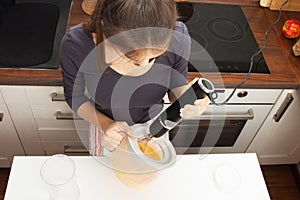 Girl beats with a mixer chicken eggs with sugar in a bowl in the kitchen