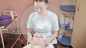 Girl beautician in a mask and gloves makes a salubrious facial massage to an attractive woman. New generation