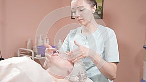 Girl beautician in a mask and gloves makes a salubrious facial massage to an attractive woman. New generation