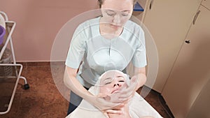 Girl beautician in a mask and gloves makes a salubrious facial massage to an attractive woman. New generation