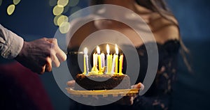 Girl in a beautiful black dress holds a cake in her hands and a man lights candles on a birthday cake. concept of