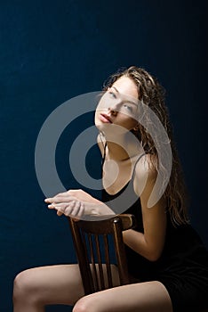 A girl with beautiful bright skin sits on a wooden chair, wet curly hair lies on her shoulders