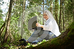 Girl with beautiful dreadlocks and laptop in green forest in spring or summer. Young IT woman, blogger working alone