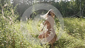 A girl in a beautiful long dress is spinning in the rays of sunlight in the forest.  The girl smiles looking at the camera. Summer