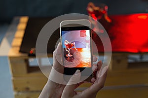 Girl with beautiful manicure photographs a snake in a glass against a dark background. the photo via phone