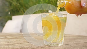 a girl with a beautiful manicure on a sunny day pours orange jamu a natural antibiotic into a glass glass with ice. A