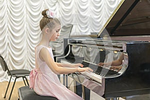 girl in a beautiful pink dress playing on a black grand piano. Girl playing on a black piano.
